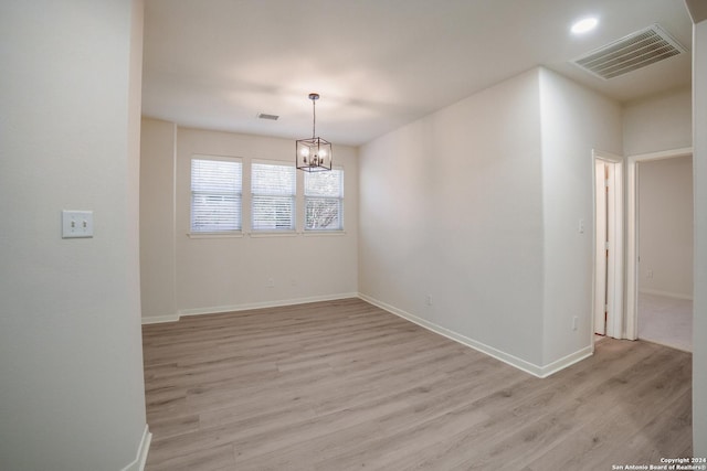 empty room featuring light wood-type flooring and an inviting chandelier