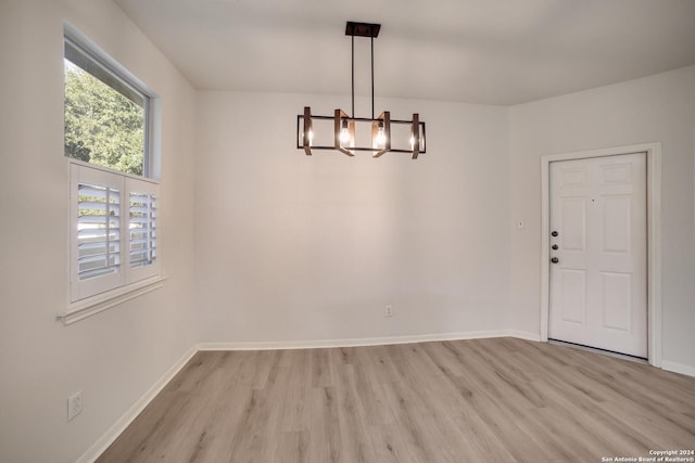 unfurnished dining area featuring light wood-type flooring and an inviting chandelier