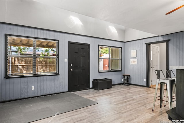 foyer entrance with ceiling fan, wood walls, lofted ceiling, and light hardwood / wood-style flooring