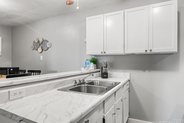 kitchen featuring a textured ceiling, kitchen peninsula, white cabinetry, and sink