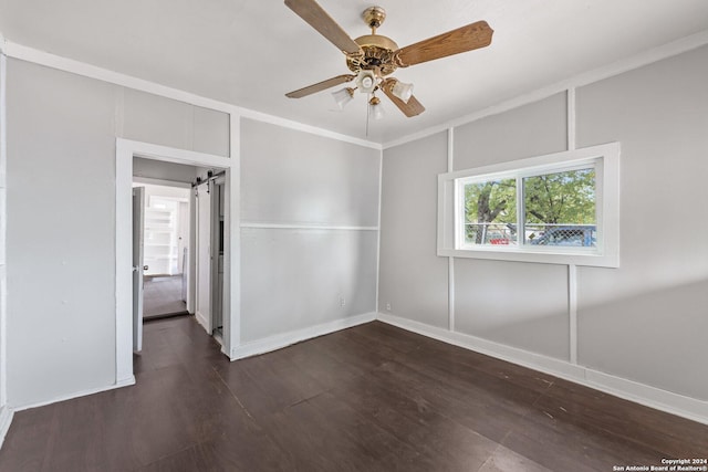 spare room featuring dark hardwood / wood-style floors, a barn door, ornamental molding, and ceiling fan