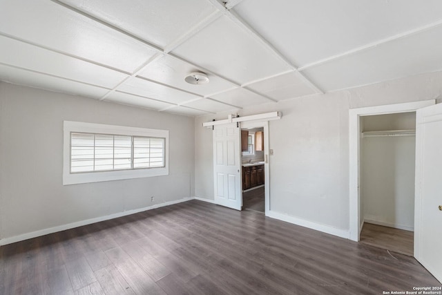 unfurnished bedroom featuring a barn door, a closet, dark wood-type flooring, and sink