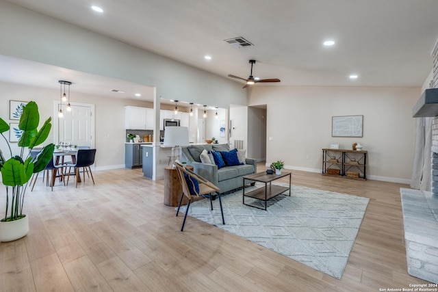 living room with a fireplace, light hardwood / wood-style flooring, ceiling fan, and lofted ceiling