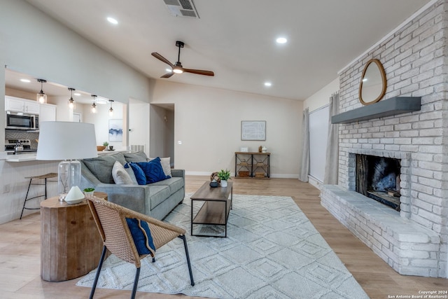 living room featuring ceiling fan, a fireplace, lofted ceiling, and light wood-type flooring