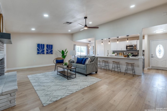 living room featuring lofted ceiling, sink, light hardwood / wood-style flooring, a brick fireplace, and ceiling fan