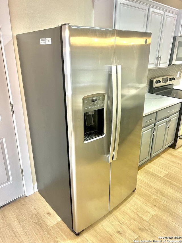 kitchen with appliances with stainless steel finishes, light hardwood / wood-style floors, and tasteful backsplash