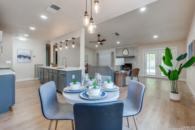 dining room featuring french doors, ceiling fan, sink, a fireplace, and light hardwood / wood-style floors