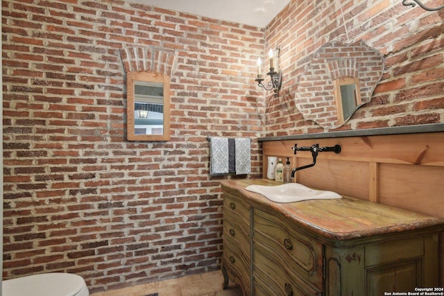 bathroom with vanity, toilet, and brick wall