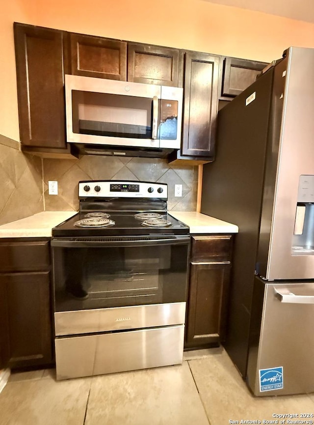 kitchen featuring backsplash, dark brown cabinets, light tile patterned flooring, and appliances with stainless steel finishes