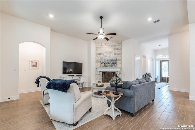 living room with a stone fireplace, ceiling fan, and light wood-type flooring