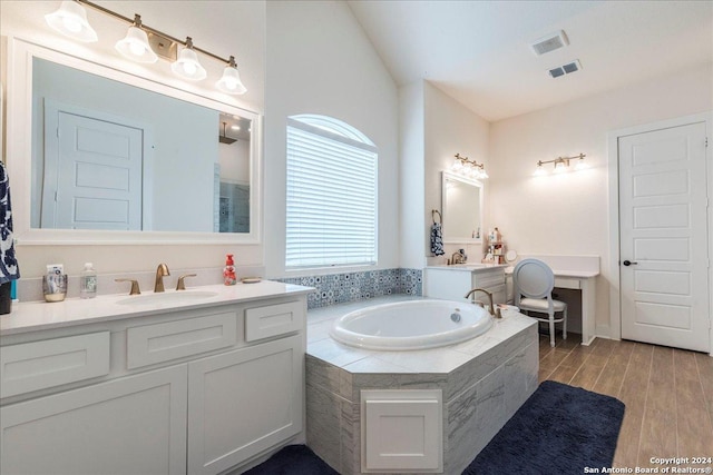 bathroom with tiled tub, vanity, and wood-type flooring