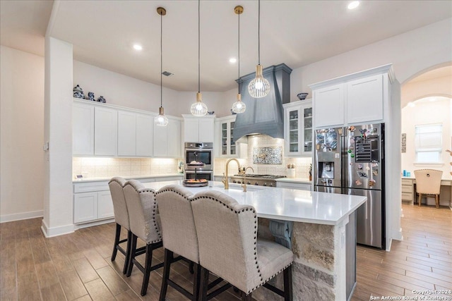 kitchen featuring white cabinets, appliances with stainless steel finishes, light wood-type flooring, and a center island with sink