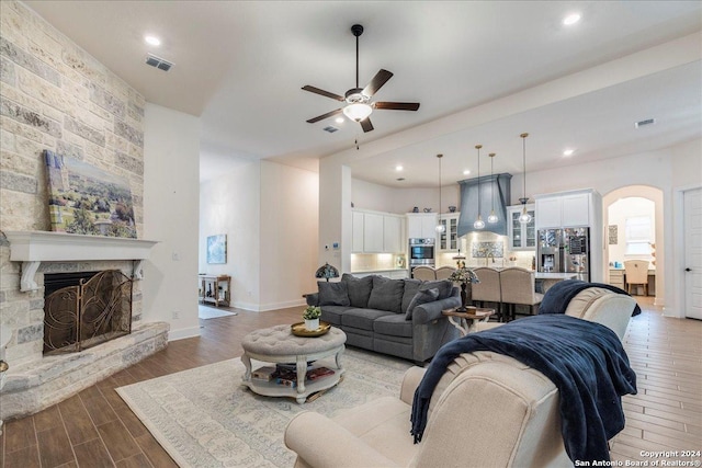 living room with a stone fireplace, ceiling fan, and wood-type flooring