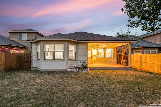 back house at dusk with a lawn, ceiling fan, and a patio