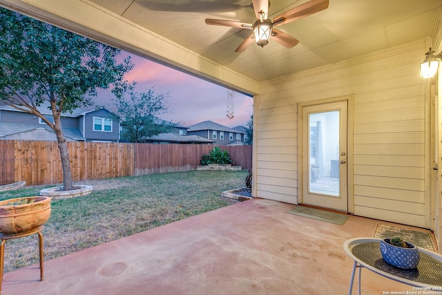 patio terrace at dusk featuring ceiling fan and a yard