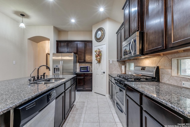 kitchen featuring decorative light fixtures, stainless steel appliances, dark stone counters, and sink