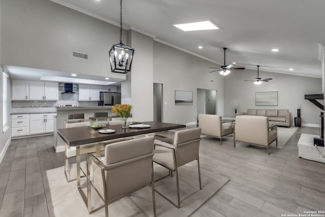 dining room with ceiling fan with notable chandelier, light wood-type flooring, crown molding, and high vaulted ceiling