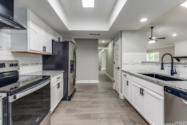 kitchen featuring wall chimney range hood, sink, light stone countertops, appliances with stainless steel finishes, and white cabinetry