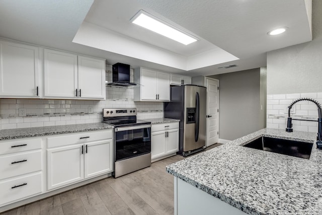 kitchen featuring sink, wall chimney exhaust hood, stainless steel appliances, white cabinets, and light wood-type flooring