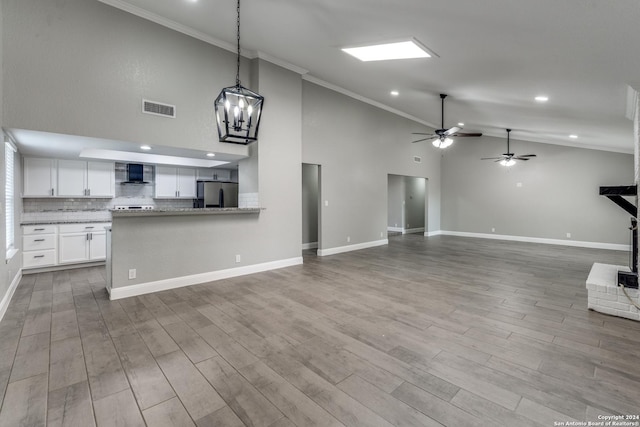 unfurnished living room with high vaulted ceiling, ornamental molding, ceiling fan with notable chandelier, and light wood-type flooring