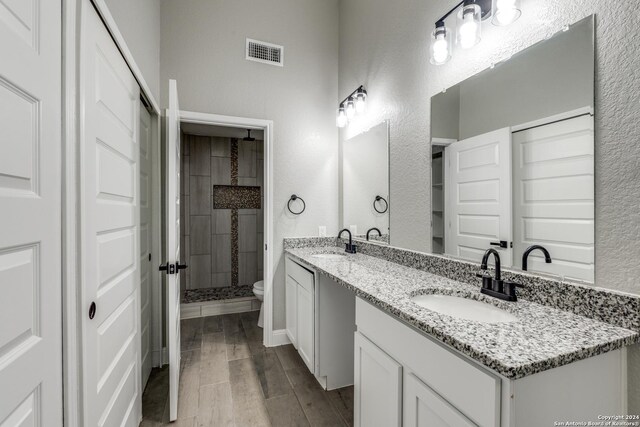 bathroom featuring toilet, a tile shower, wood-type flooring, and vanity