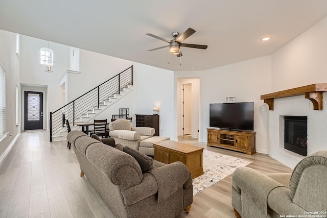 living room featuring a brick fireplace, ceiling fan with notable chandelier, a towering ceiling, and light hardwood / wood-style flooring