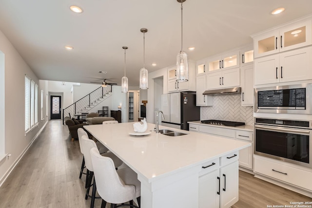 kitchen featuring appliances with stainless steel finishes, ceiling fan, a kitchen island with sink, sink, and white cabinets