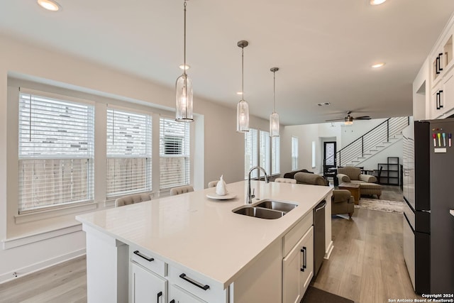 kitchen with light wood-type flooring, sink, a center island with sink, white cabinetry, and hanging light fixtures