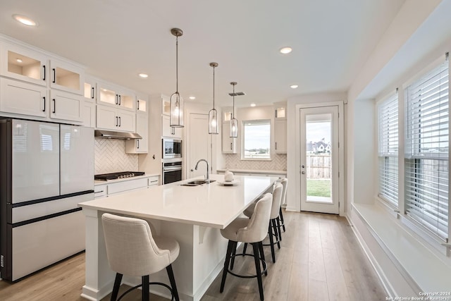 kitchen with white cabinetry, backsplash, a kitchen island with sink, appliances with stainless steel finishes, and light wood-type flooring