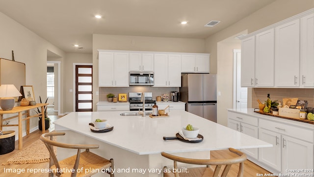 kitchen featuring a center island with sink, decorative backsplash, white cabinetry, and appliances with stainless steel finishes