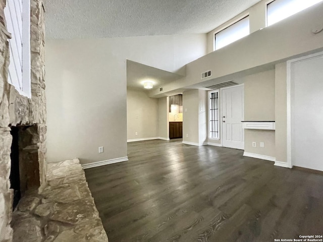 unfurnished living room featuring a fireplace, a textured ceiling, high vaulted ceiling, and dark wood-type flooring