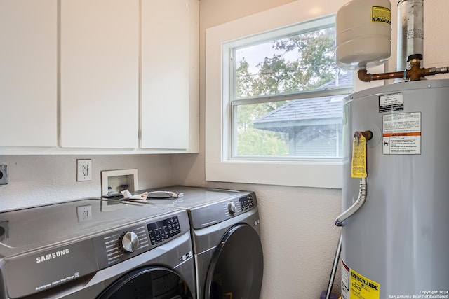 clothes washing area featuring cabinets, washing machine and clothes dryer, and water heater