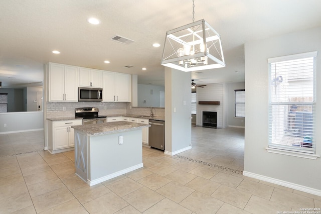 kitchen featuring sink, decorative light fixtures, a fireplace, white cabinets, and appliances with stainless steel finishes