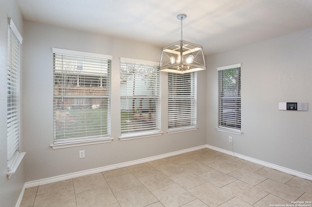 unfurnished dining area with a wealth of natural light, light tile patterned floors, and a chandelier