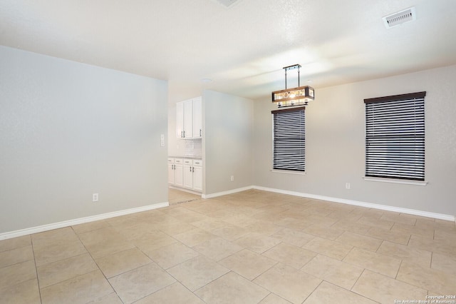 spare room with a notable chandelier and light tile patterned flooring