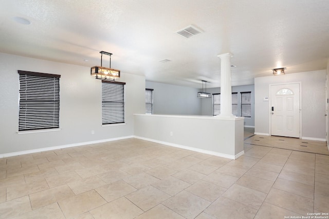 spare room featuring decorative columns, light tile patterned floors, and a textured ceiling