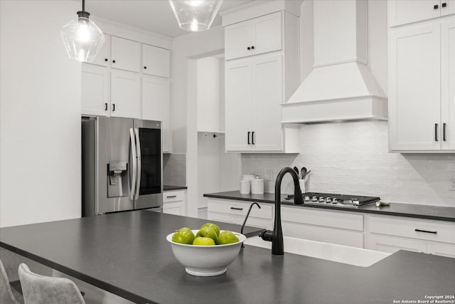 kitchen with decorative backsplash, appliances with stainless steel finishes, custom exhaust hood, pendant lighting, and white cabinets