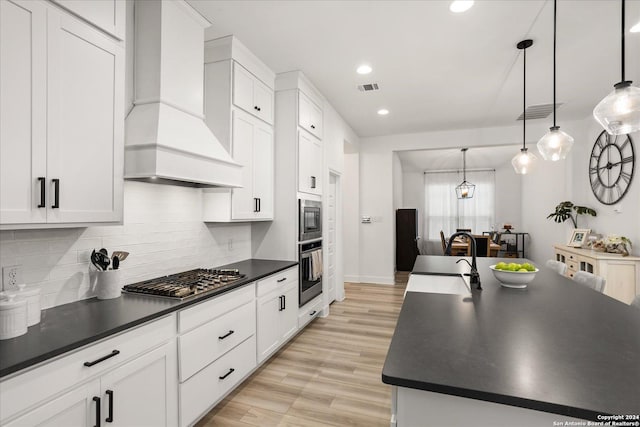 kitchen featuring a center island with sink, appliances with stainless steel finishes, pendant lighting, and custom exhaust hood