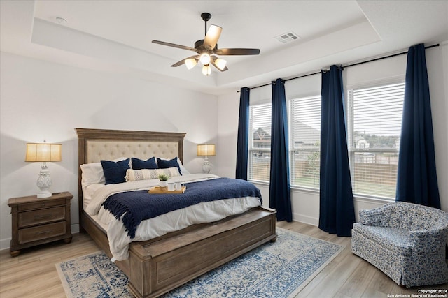 bedroom featuring ceiling fan, light hardwood / wood-style flooring, and a tray ceiling