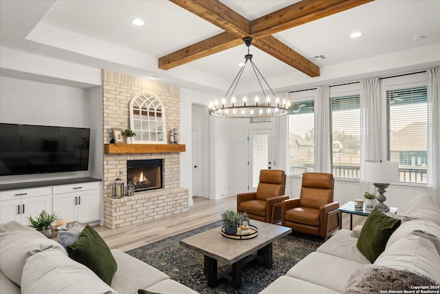 living room with a fireplace, light hardwood / wood-style floors, a chandelier, and beamed ceiling