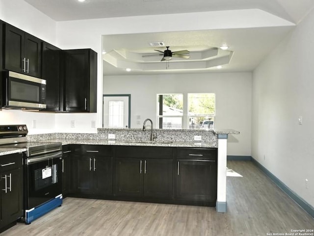 kitchen with a tray ceiling, electric stove, ceiling fan, and sink