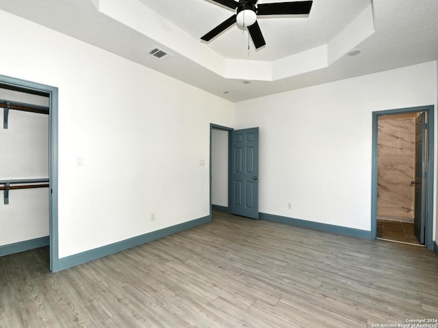 unfurnished bedroom featuring a raised ceiling, ceiling fan, a closet, and wood-type flooring