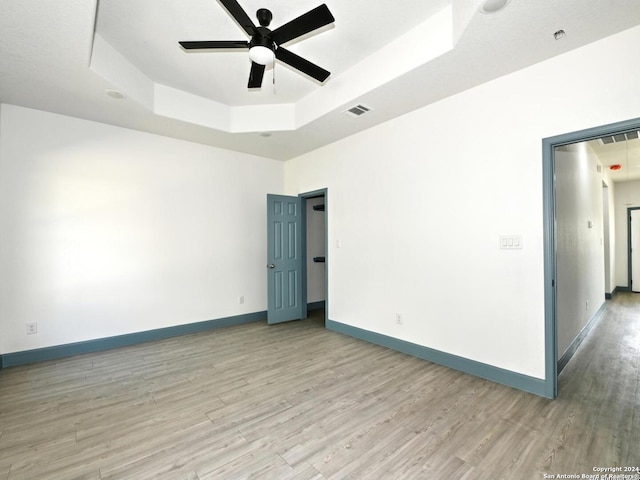 unfurnished room featuring a tray ceiling, light hardwood / wood-style flooring, and ceiling fan