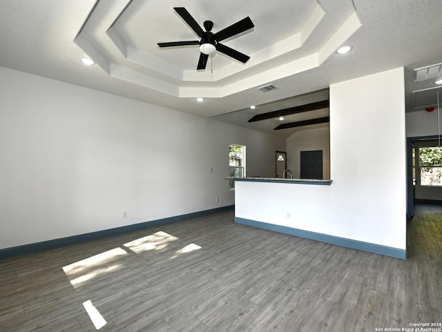 unfurnished living room with a textured ceiling, a tray ceiling, ceiling fan, and dark wood-type flooring