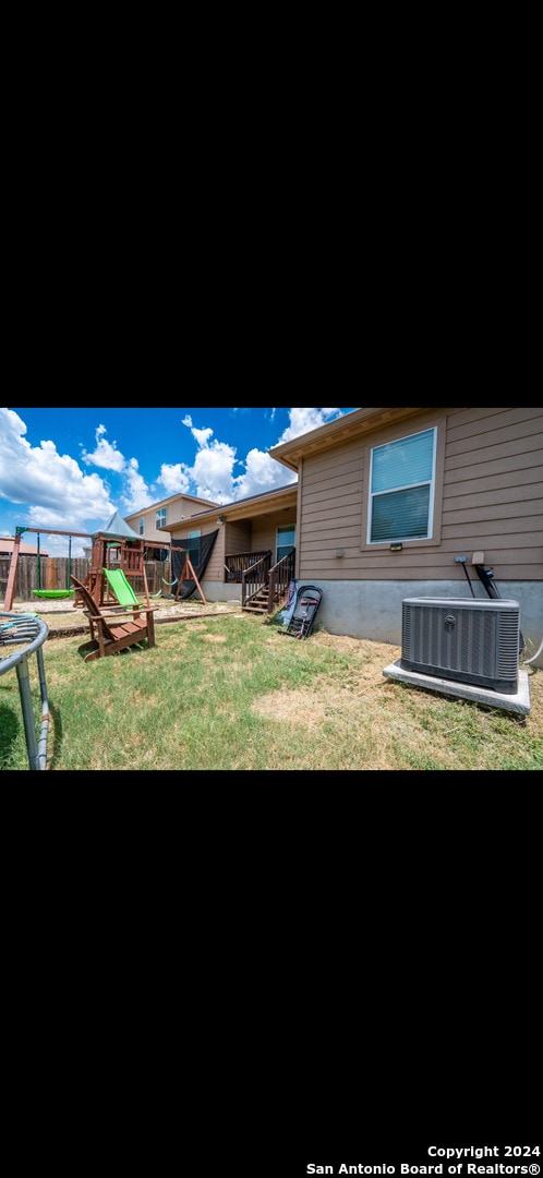 rear view of house with a playground, central AC, a lawn, and a trampoline