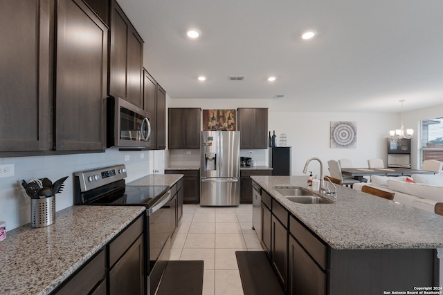 kitchen with dark brown cabinetry, sink, a notable chandelier, an island with sink, and appliances with stainless steel finishes