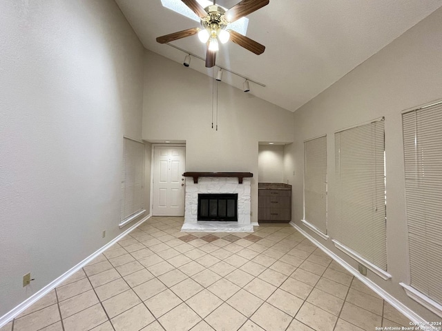 unfurnished living room with high vaulted ceiling, track lighting, a stone fireplace, ceiling fan, and light tile patterned floors