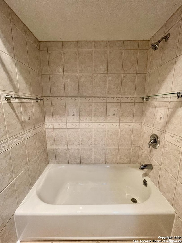 bathroom featuring a textured ceiling and tiled shower / bath