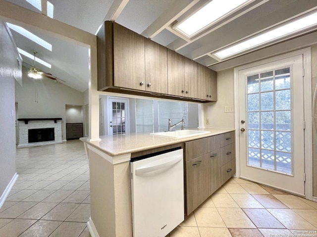 kitchen with dishwasher, lofted ceiling, sink, a brick fireplace, and light tile patterned floors