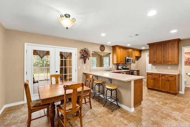 kitchen featuring kitchen peninsula, french doors, appliances with stainless steel finishes, a kitchen breakfast bar, and sink